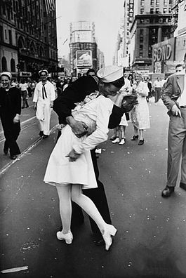 A sailor kissing a nurse in a street celebration, surrounded by a crowd in a city setting, captured in black and white.